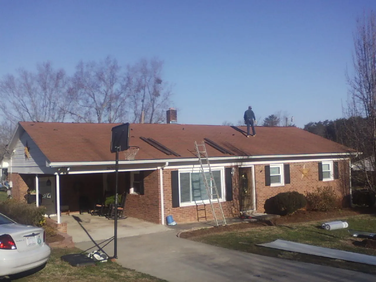 Roofer stripping a shingle roof on a brick ranch before metal panels in Belmont